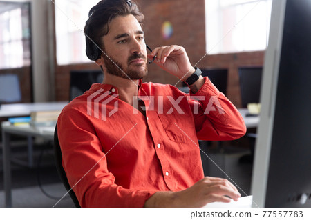 Portrait of caucasian businessman sitting at desk wearing headset having video call 77557783