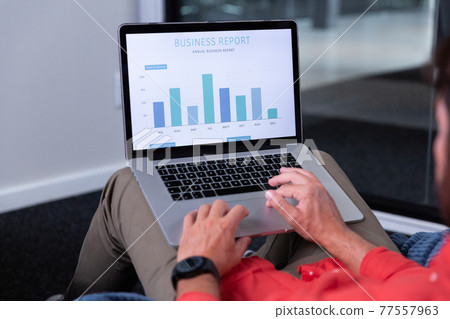 Midsection of caucasian businessman sitting on bean bag and making charts on laptop 77557963