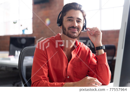 Portrait of caucasian businessman sitting at desk wearing headset having video call 77557964