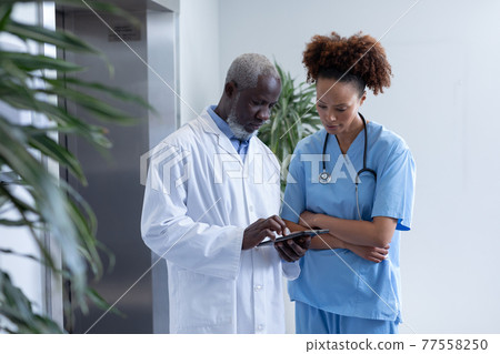 Diverse male and female doctors using tablet and discussing in hospital corridor 77558250