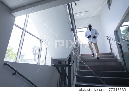 Senior african american male doctor wearing lab coat running down stairs in hospital 77558283