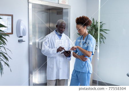 Diverse male and female doctors using tablet and discussing in hospital corridor 77558304
