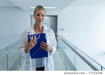 Portrait of caucasian female doctor standing in hospital corridor holding medical chart document 77558306