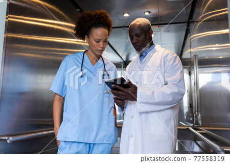 Serious diverse female and male doctors using tablet in hospital lift 77558319