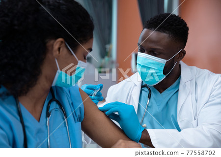 Mixed race couple of doctors wearing face masks making injection Mixed race couple of doctors wearing face masks making injection 77558702
