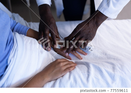 Midsection of african american male doctor putting oximeter on finger of patient in hospital bed Midsection of african american male doctor putting oximeter on finger of patient in hospital bed 77559611