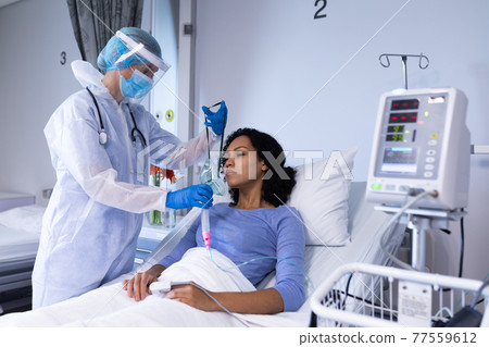 Caucasian female doctor in ppe suit putting ventilator on african american female patient Caucasian female doctor in ppe suit putting ventilator on african american female patient 77559612
