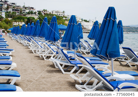 Rows of empty blue sun loungers and umbrellas on the beach. Camel Beach in Turkey. Rows of empty blue sun loungers and umbrellas on the beach. Camel Beach in Turkey. 77560045