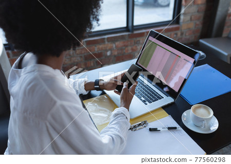 African american woman sitting in cafe using smartphone and laptop 77560298