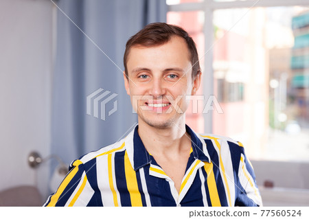 Attractive young man in a striped shirt at home Attractive young man in a striped shirt at home 77560524