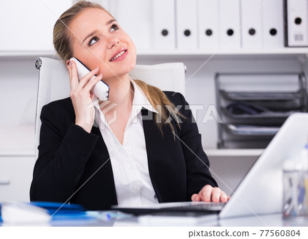 Woman talking on phone in office 77560804