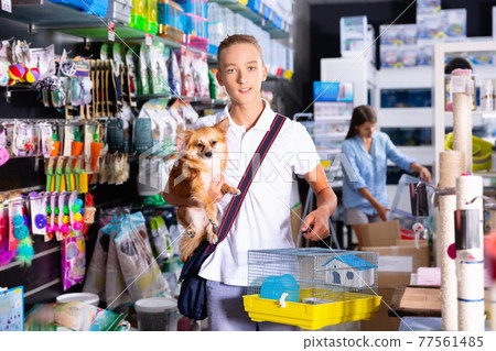 Teen boy with dog is looking a cage for canary bird in pet shop 77561485