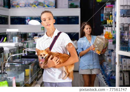 Young man with dog standing near aquarium in pet shop 77561747