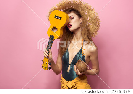 Woman holding ukulele coconut cocktail beach hat Exotic lifestyle swimsuit pink background 77561959