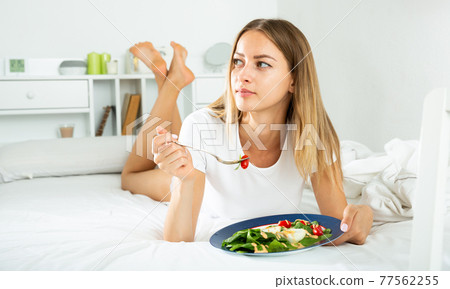 Cheerful young girl in lingerie having a salad while laying in the bed 77562255