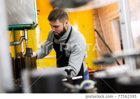 Guy working on olive oil bottling conveyor Guy working on olive oil bottling conveyor 77562395
