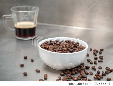 Roasted coffee beans in white bowl with americano in glass cup on table 77565381