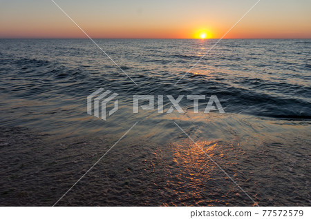 The sun is setting behind the sea horizon. Sunset on the seashore. The sun is setting behind the sea horizon. Sunset on the seashore. 77572579