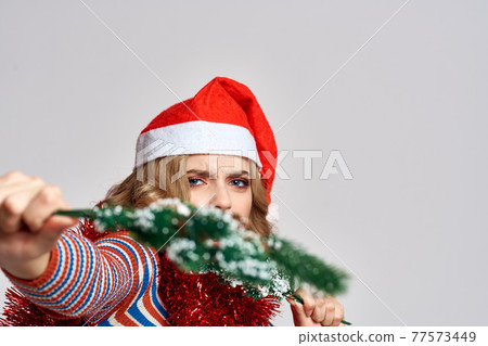 emotional woman with branches of a festive tree and red tinsel cap on her head striped sweate 77573449