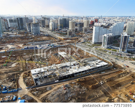 Drone view of a large construction site. Tower cranes in action on fog background. Drone view of a large construction site. Tower cranes in action on fog background. 77573893