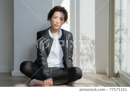 Genderless LGBT young woman in a leather jacket sitting on the floor 77575101