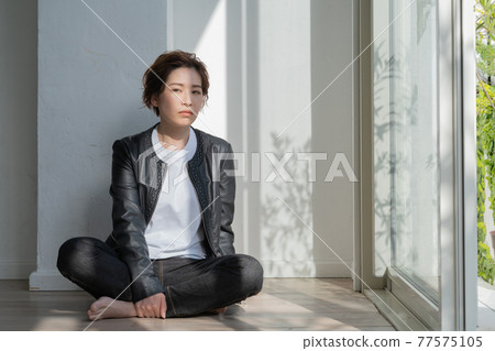 Genderless LGBT young woman in a leather jacket sitting on the floor Genderless LGBT young woman in a leather jacket sitting on the floor 77575105