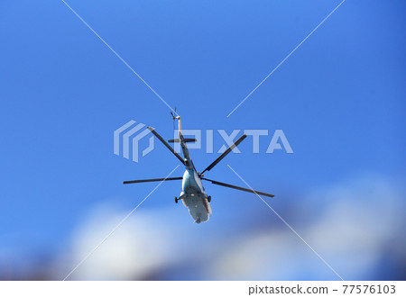 Helicopter flies in the air against a blue sky Helicopter flies in the air against a blue sky 77576103