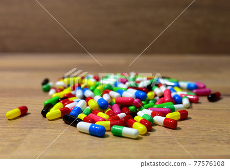 Pills in multicolored capsules on wooden background.  77576108