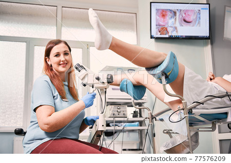 Smiling gynecologist examining female patient with colposcope. 77576209