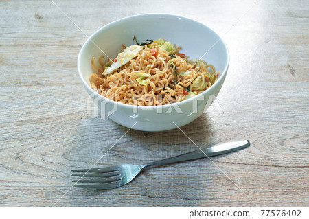 spicy fried instant noodles with cabbage and basil leaf on white bowl 77576402