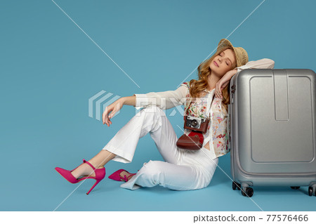Happy woman in blouse and trousers sitting near suitcase Happy woman in blouse and trousers sitting near suitcase 77576466