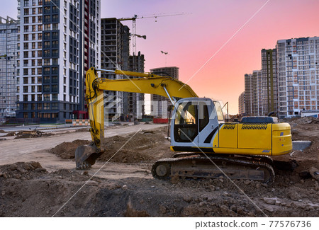 Excavator during earthmoving work at construction site on sunset background. Excavator during earthmoving work at construction site on sunset background. 77576736