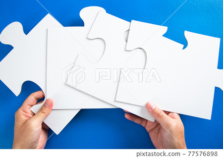 man hands holding big paper white blank puzzles on a blue background, concept of business 77576898