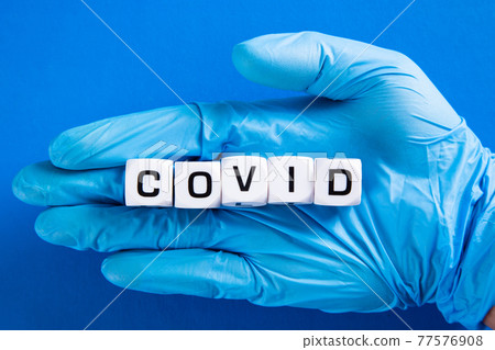 Hand in blue glove with Covid word. COVID-19 pandemic concept. Hand in blue glove with Covid word. COVID-19 pandemic concept. 77576908
