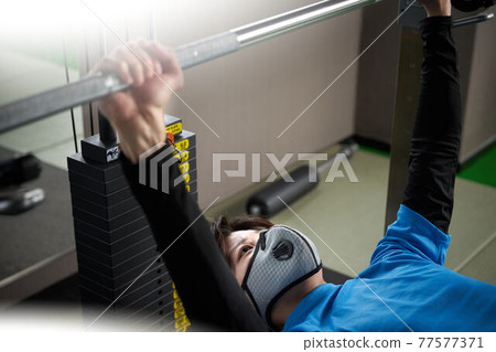 Young man wearing a mask and doing weight training 77577371