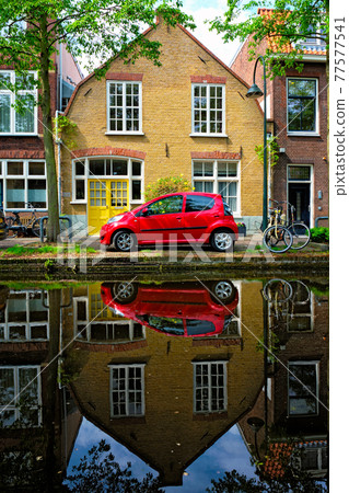 Red car on canal embankment in street of Delft. Delft, Netherlands 77577541