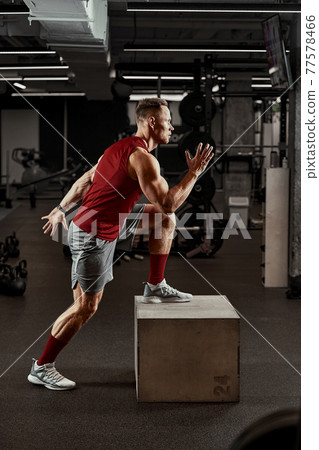Sexy muscular men using the platform for his legs on a dark colorful background of gym. Sexy muscular men using the platform for his legs on a dark colorful background of gym. 77578466