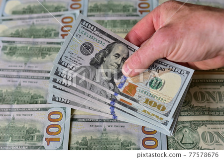 Stack Of 100 Dollars Banknotes Bundles in a man's hand against the background of American banknotes Stack Of 100 Dollars Banknotes Bundles in a man's hand against the background of American banknotes 77578676