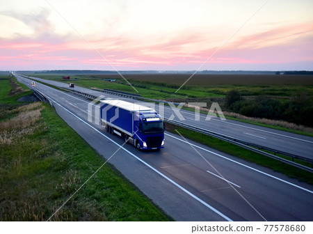 Truck with semi-trailer driving along highway on the sunset background. Truck with semi-trailer driving along highway on the sunset background. 77578680