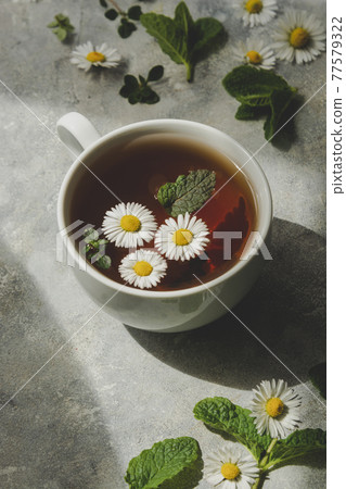 Cup of herbal tea with chamomile flowers and mint leaves 77579322