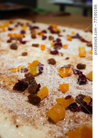 A pastry chef spreads candied fruit, raisins and chocolate pieces on puff pastry. Making dough curls. The job of a pastry chef. Making desserts 77580166