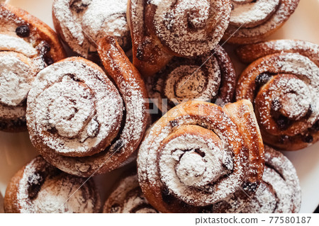 Puff pastry cakes curl with powdered sugar on top. A close-up of a bakery product. Confectionery work and customer service. A treat on a tray. 77580187