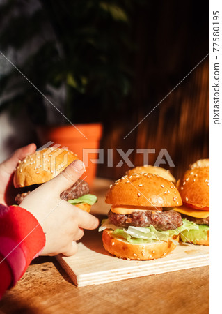 Mini burger on a stand close-up. Children fast food in a restaurant or cafe. Macro photo of burger ingredients with meat and vegetables. Eco burgers for children 77580195