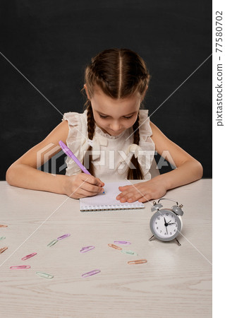 cute little child girl reading a book in the classroom on background of blackboard. Back to school. 77580702