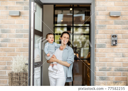 Housewife with newborn baby staying in front of entrance door 77582235