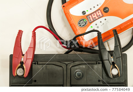 Recharging the car battery with red and black copper clips attached to the terminals. 77584049