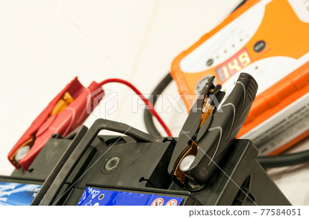 Recharging the car battery with red and black copper clips attached to the terminals. 77584051