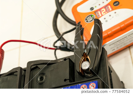 Recharging the car battery with red and black copper clips attached to the terminals. 77584052