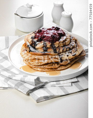 Food still life. Close-up a stack of delicious hot pancakes with chocolate and raspberry jam. Traditional delicious dessert or sweet breakfast on a white plate on a light table. Vertical shot 77584459