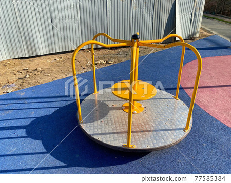 Children's round metal blue swing carousel for sports games in the courtyard of a new building on a children's playground Children's round metal blue swing carousel for sports games in the courtyard of a new building on a children's playground 77585384